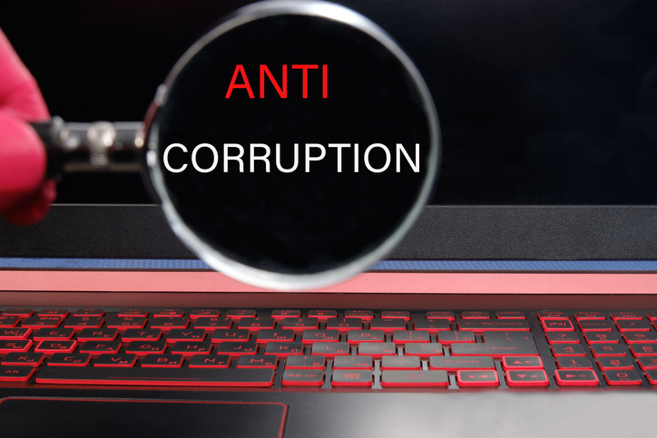 Anti corruption text with magnifying glass over laptop keyboard